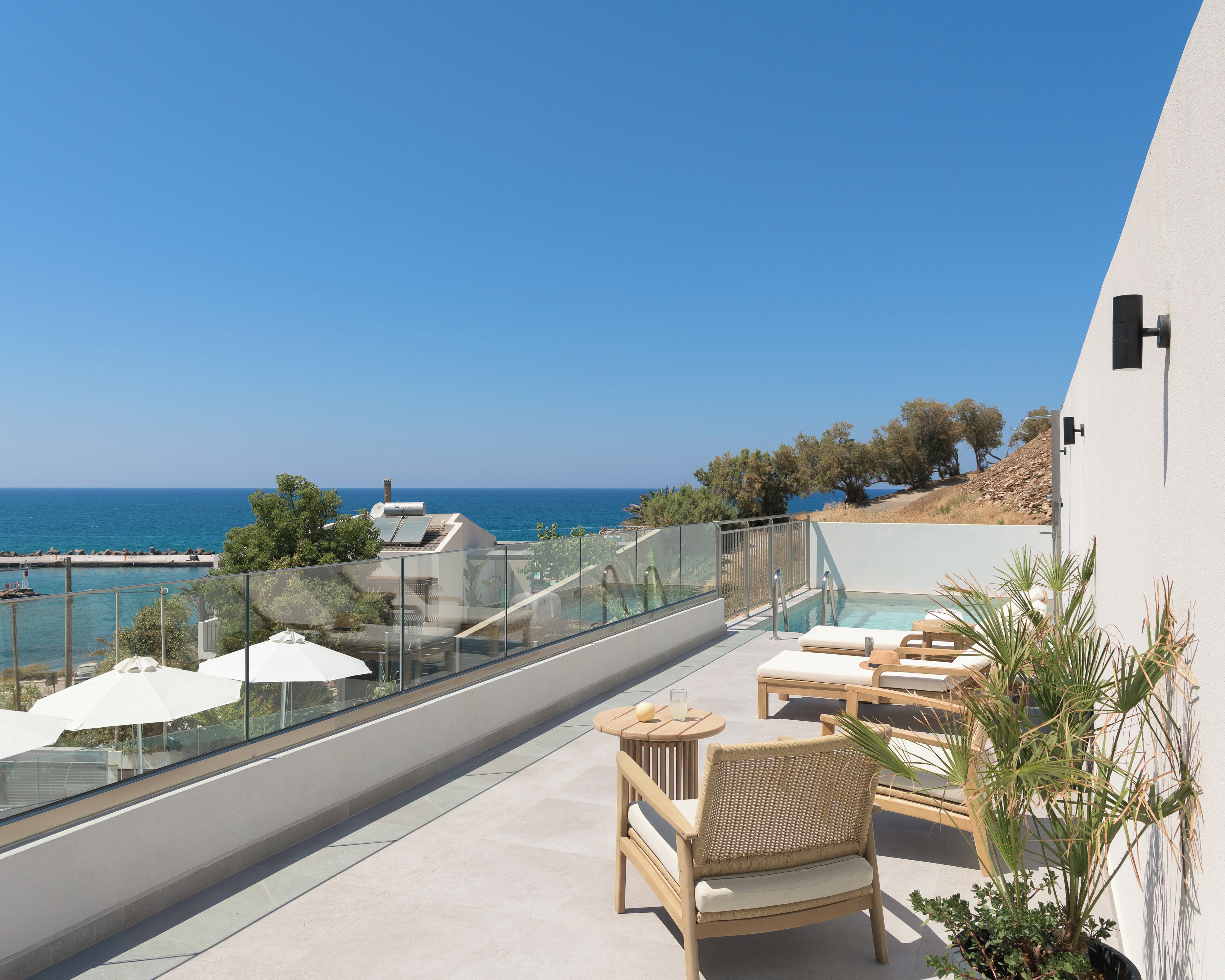 A balcony with a pool, lounge chairs, and a view of the sea.