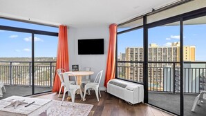 A balcony with a table and chairs, a flat-screen TV, and a view of buildings. - Ocean View Corner King Suite Sleeps 4 (Myrtle Beach)