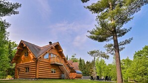 Een vakantiehuis in blokhutstijl met een balkon, een trap en uitzicht op het omliggende bos.