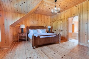 A wooden-paneled room with a bed, two bedside tables, and a chandelier. - Fiddler Lake Resort - Moose 89 (Mille-Isles)