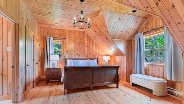 Een slaapkamer met houten lambrisering, een bed, nachtkastjes, een bankje en een kroonluchter.