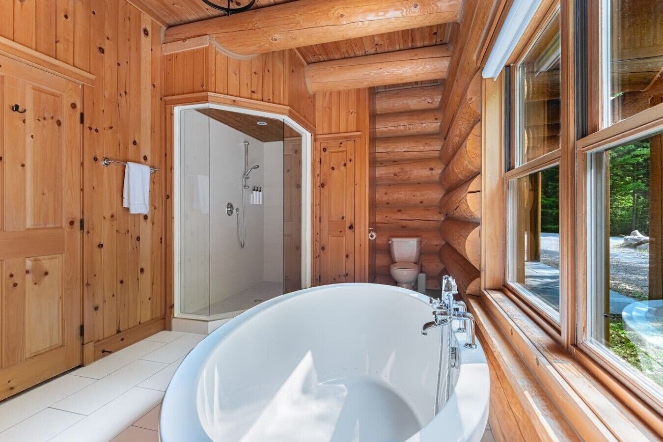 Ein Badezimmer einer Holzhütte mit einer großen Badewanne, einer Dusche und einem WC.