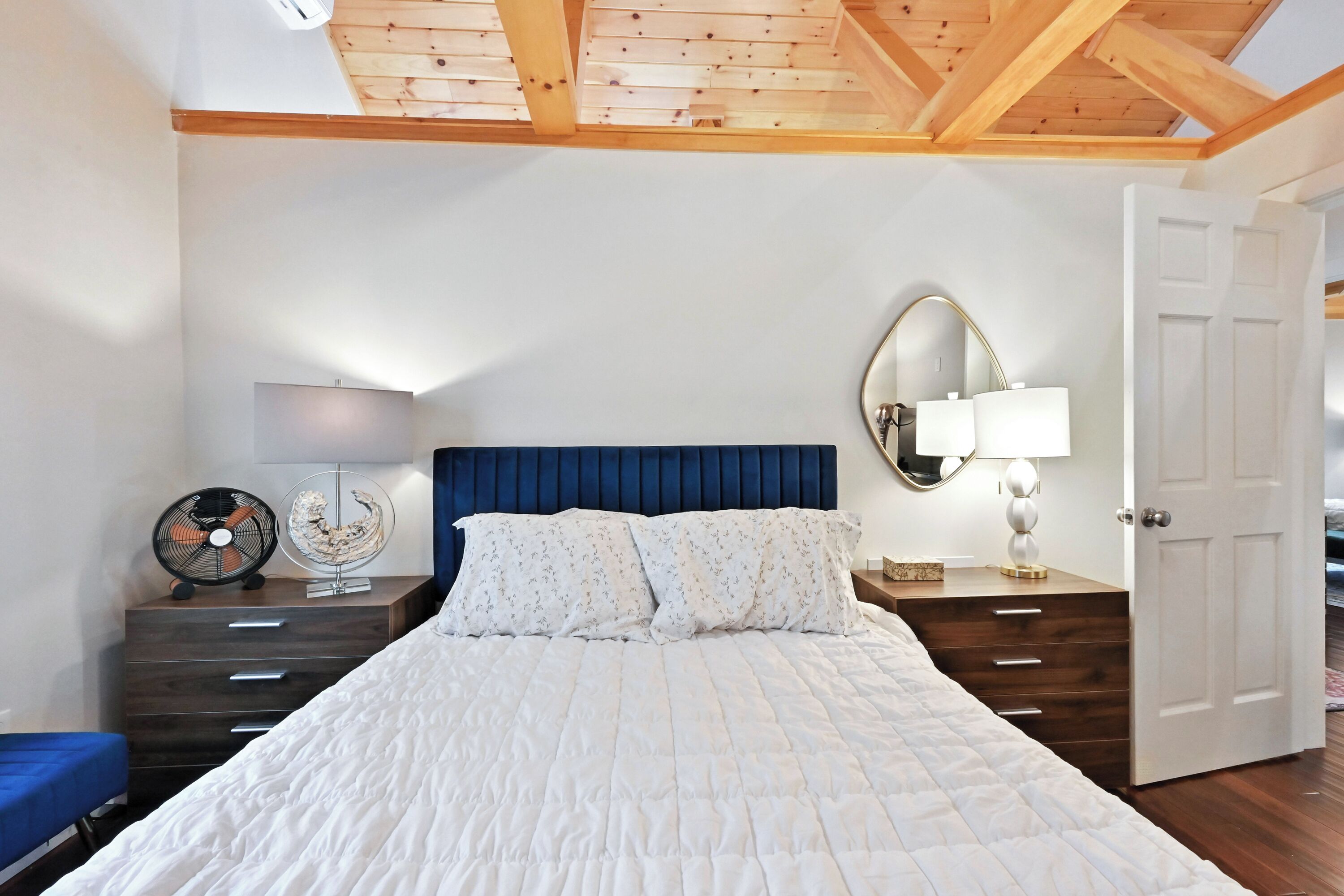 A bedroom with a large bed, wooden headboard, two bedside tables with lamps, a mirror, and a door.