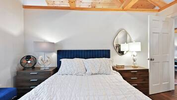 A bedroom with a large bed, wooden headboard, two bedside tables with lamps, a mirror, and a door.