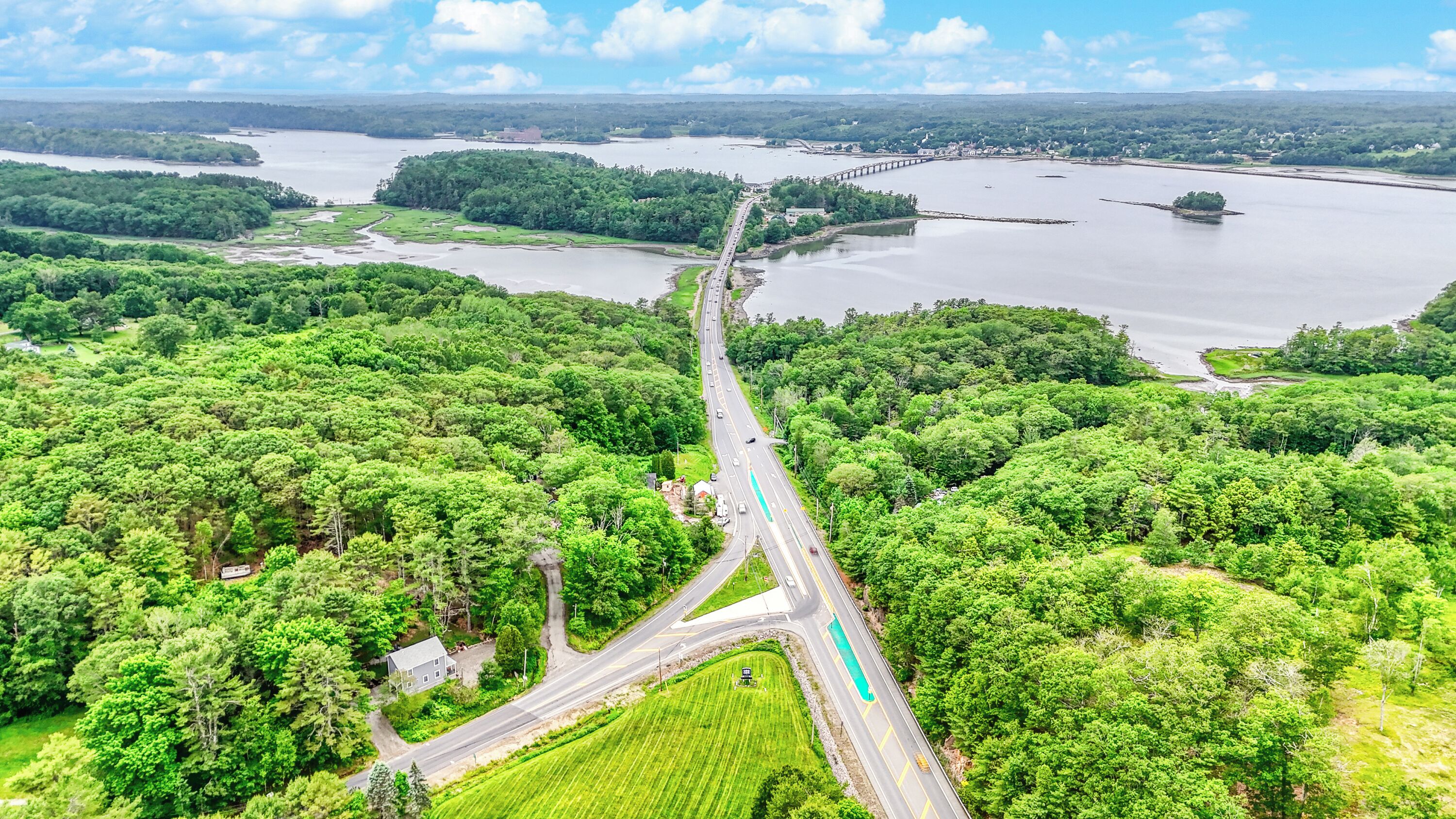 Une vue aérienne d’une autoroute qui serpente à travers une zone densément boisée, avec une rivière et un pont en arrière-plan.