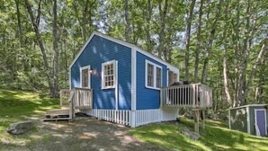 A small blue cabin with a wooden deck and a porch, surrounded by trees. - Happy Cottage Near Everything 11 (Edgecomb)