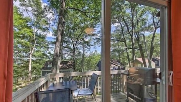 A deck with a table and chairs, overlooking a wooded area with trees and a house in the background. - Happy Cottage Near Everything 11 (Edgecomb)