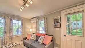A room with a grey sofa, a door, and a window with a view of greenery. - Happy Cottage Near Everything 11 (Edgecomb)