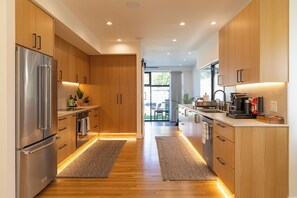 A modern kitchen with wooden cabinets, stainless steel appliances, and a central island with seating. - Private wellness home with pool, sauna, & cold plunge - in the center of Venice. (Los Angeles)