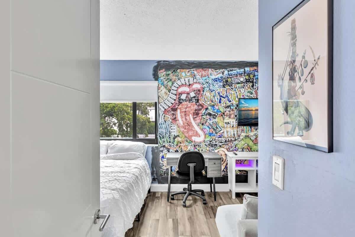 A modern bedroom with a large mural, a desk, and a bed.