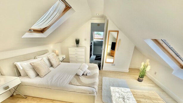 A modern bedroom with a large bed, a skylight, a small desk, and a mirror.