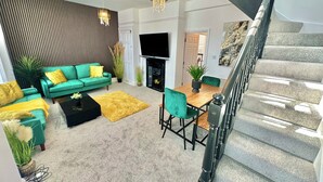 A modern living room with a green sofa, yellow cushions, a wooden coffee table, and a dining area with a wooden table and green chairs.