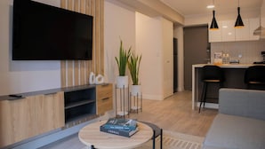 A modern living room with a flat-screen TV, wooden paneling, a round coffee table with a book, and a kitchen area with bar stools. - w* | Impressive 1BR w/ Balcony in Miraflores (Miraflores)