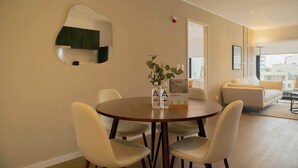 Una sala de estar moderna con una mesa de comedor redonda, sillas blancas, un sofá y un espejo grande en la pared.