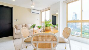A modern living room with a sofa, two white chairs with woven seats, a round table, and a potted plant. - w* | Modern 1BR in the Heart of Obarrio (Panamá)