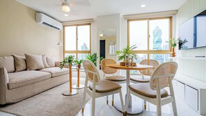 A modern living room with a sofa, round table, and chairs, large windows with a city view, and an air conditioning unit on the wall. - w* | Modern 1BR in the Heart of Obarrio (Panamá)
