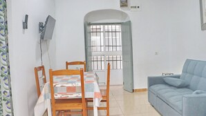 A small, clean room with a dining table, chairs, a sofa, and a window with bars. - El patio de Tarifa . (Tarifa)