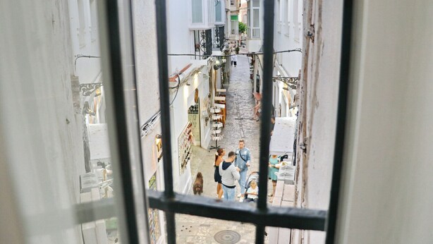 A narrow street with buildings on either side, a few pedestrians, and a dog. - El patio de Tarifa . (Tarifa)