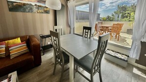 A modern living room with a dining area, a sofa with striped cushions, a table with chairs, and a large window with a view of the outdoors. - La mouette rieuse, terrace, sea view, beach access (Bernières-sur-Mer)