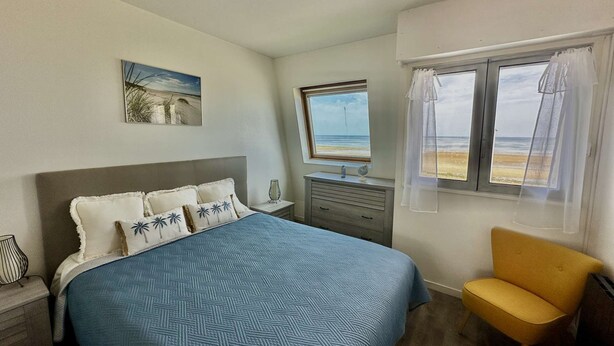 A bedroom with a bed, a chair, a nightstand, a dresser, and a window with a view of the beach. - La mouette rieuse, terrace, sea view, beach access (Bernières-sur-Mer)
