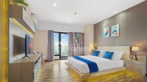 A modern hotel room with a large bed, a desk with a TV, and a balcony with a view.