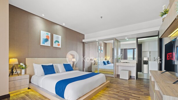 A modern hotel room with a large bed, bedside tables, a vanity with a mirror, and a television.