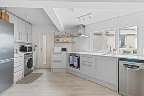A modern kitchen with white cabinets, stainless steel appliances, and a large window providing natural light. - Stunning Beachfront Bungalow  Ocean Views & BBQ (Pevensey Bay)