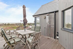 An outdoor deck with a wooden table and chairs, a flag, and a view of the sea.