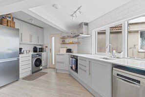A modern kitchen with white cabinetry, stainless steel appliances, and a large window providing natural light. - Stunning Beachfront Bungalow  Ocean Views & BBQ (Pevensey Bay)