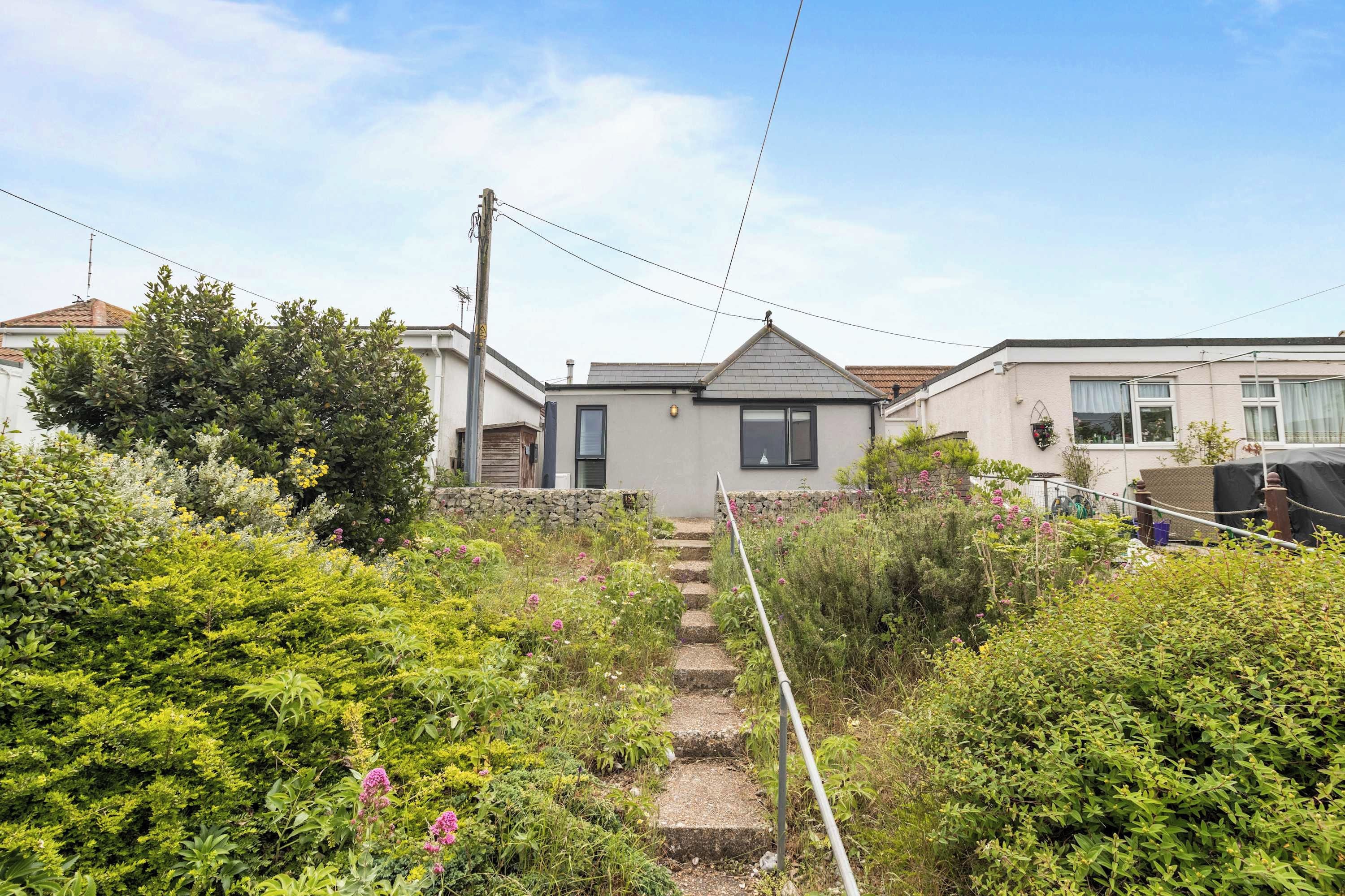 A residential property with a stone staircase leading to a house with a grey roof and a small porch.