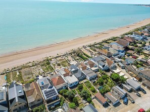 An aerial view of a coastal residential area with houses, a beach, and a clear view of the sea.