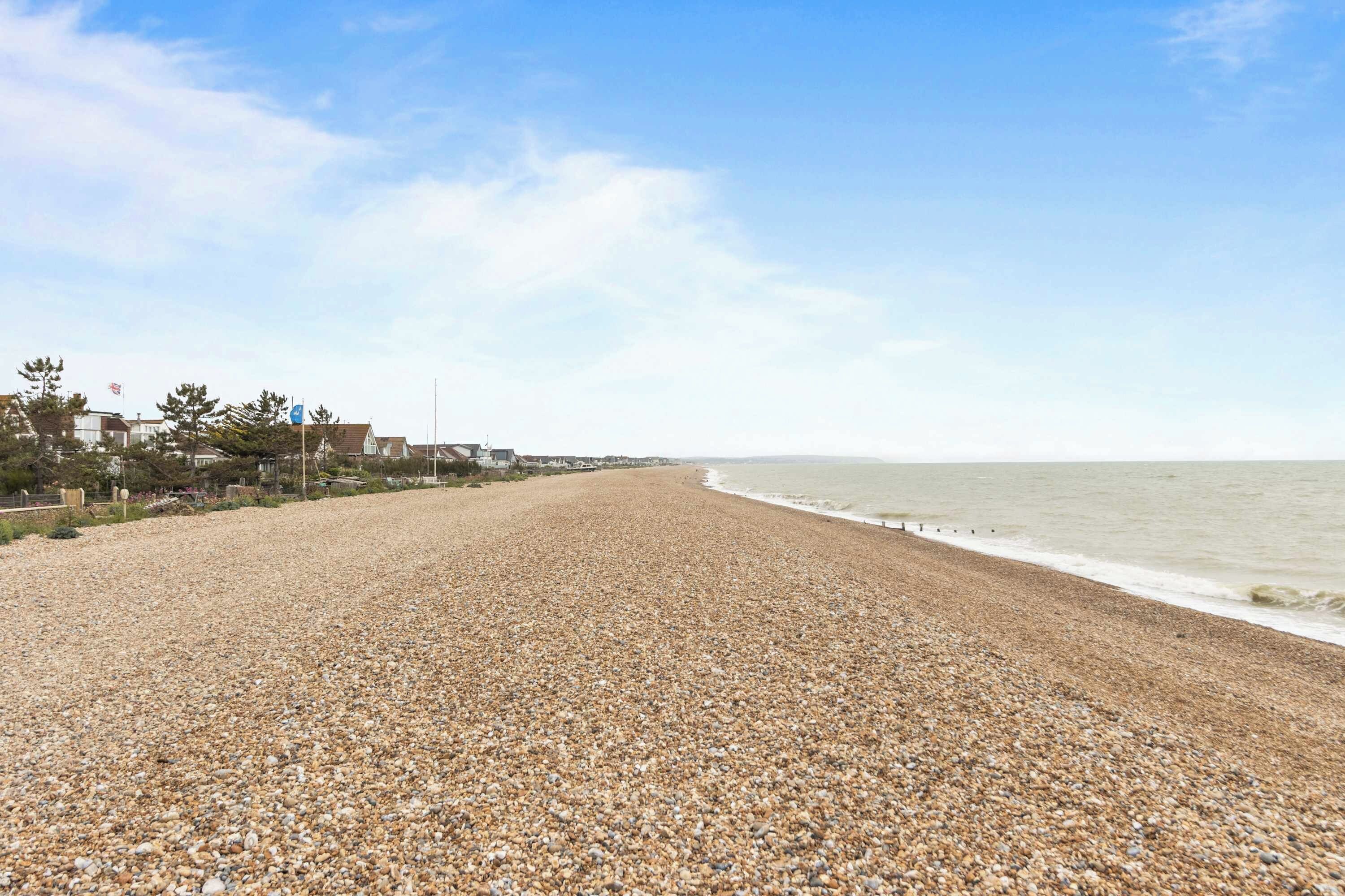 A pebbled beach with a view of the ocean and houses in the background.