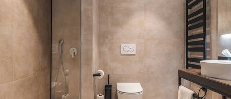 Un baño moderno con cabina de ducha de vidrio, inodoro, lavamanos y perchero para toallas.
