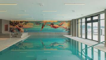 An indoor swimming pool with a mural of swimmers, large windows, and a clear view of the outside.
