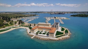 Vista aérea de una propiedad costera con un puerto deportivo, un edificio central con techo rojo y follaje circundante.
