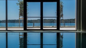 Vista a través de amplios ventanales a un área de piscina con vista despejada a la playa y árboles.