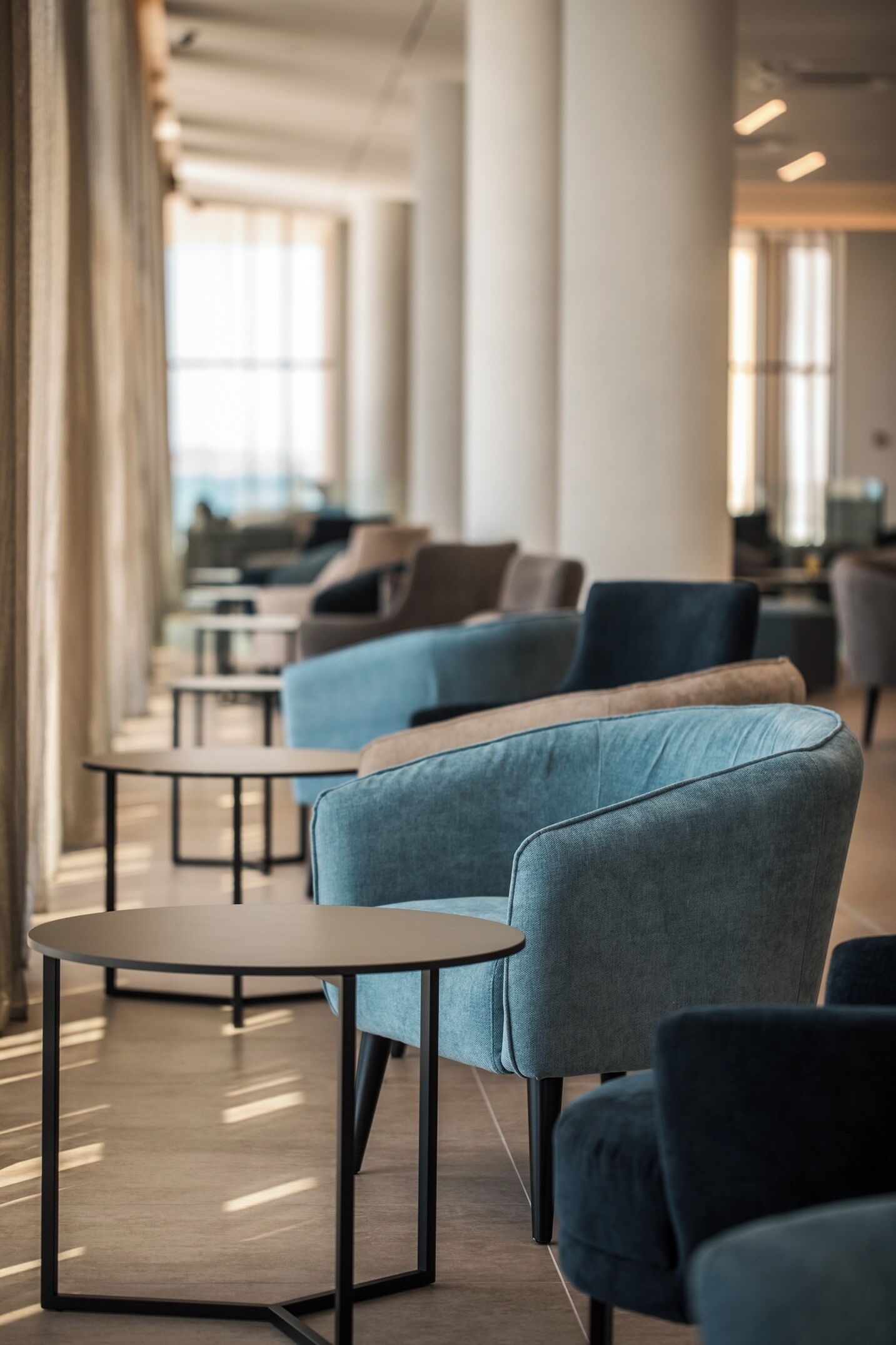 A modern lounge area with sofas and round tables, large windows, and a clean, minimalist design.