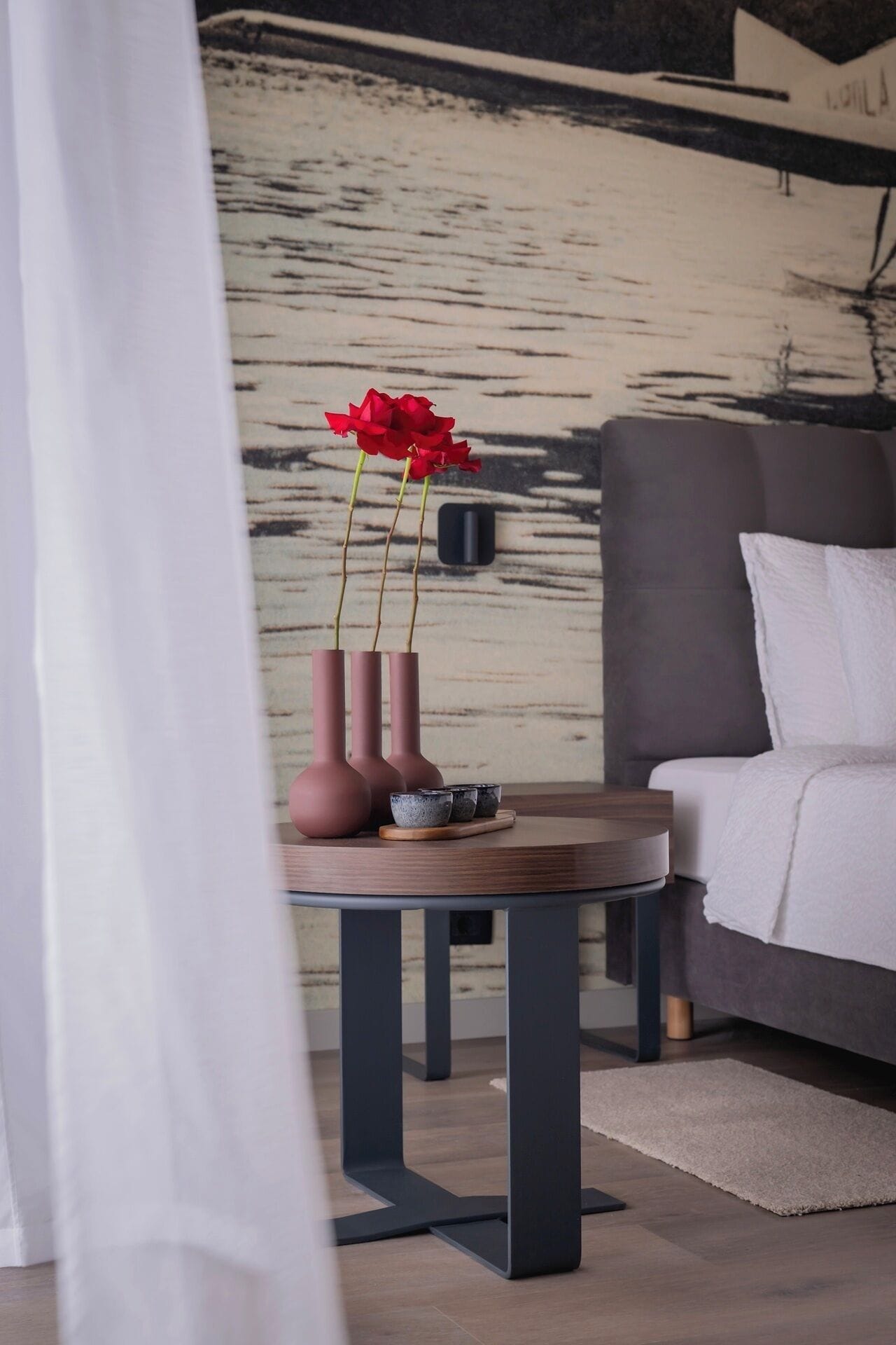 A modern living room with a grey sofa, a wooden coffee table with vases and a bowl, and a textured wall in the background.