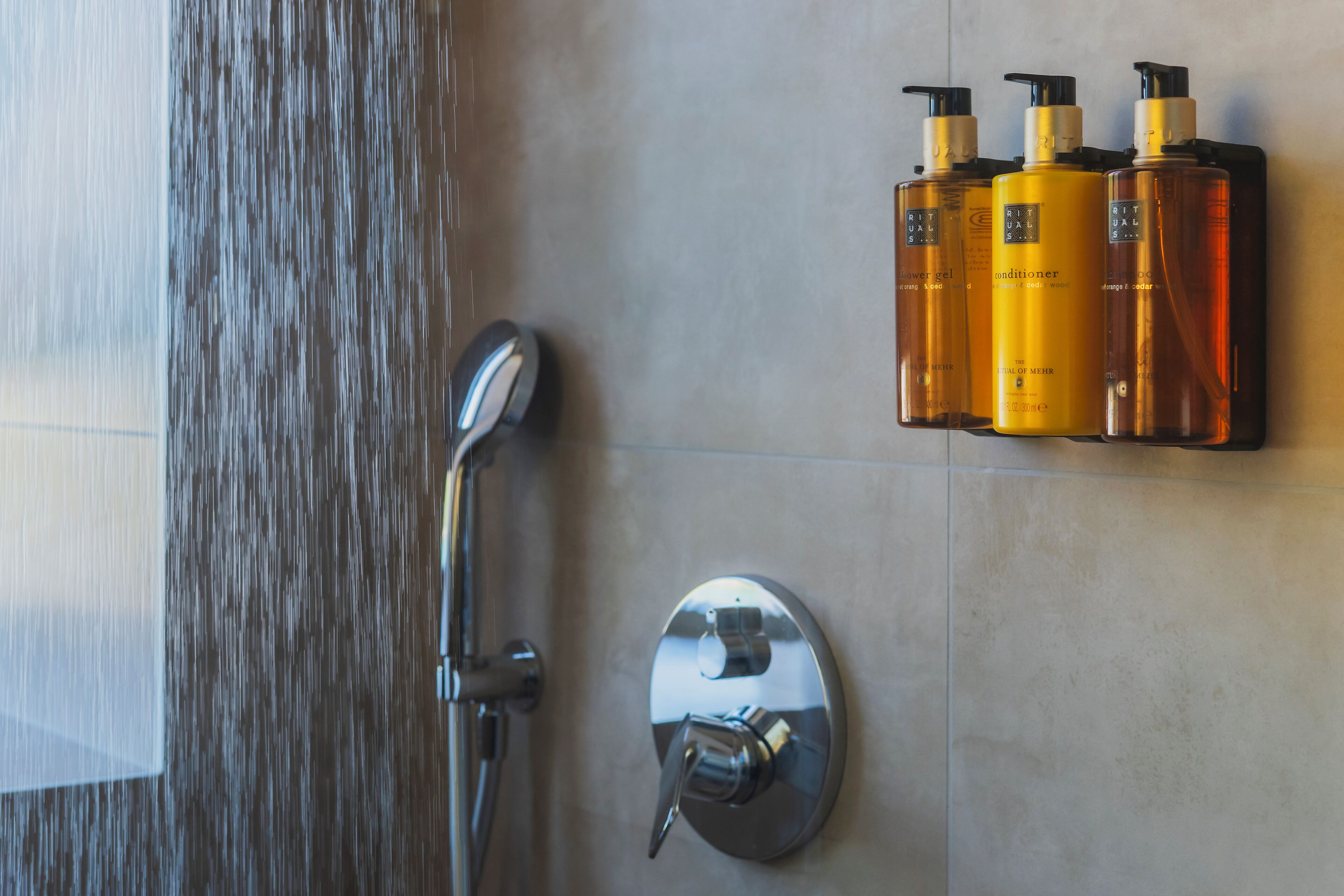 A shower with a rain showerhead and a wall-mounted soap dispenser.
