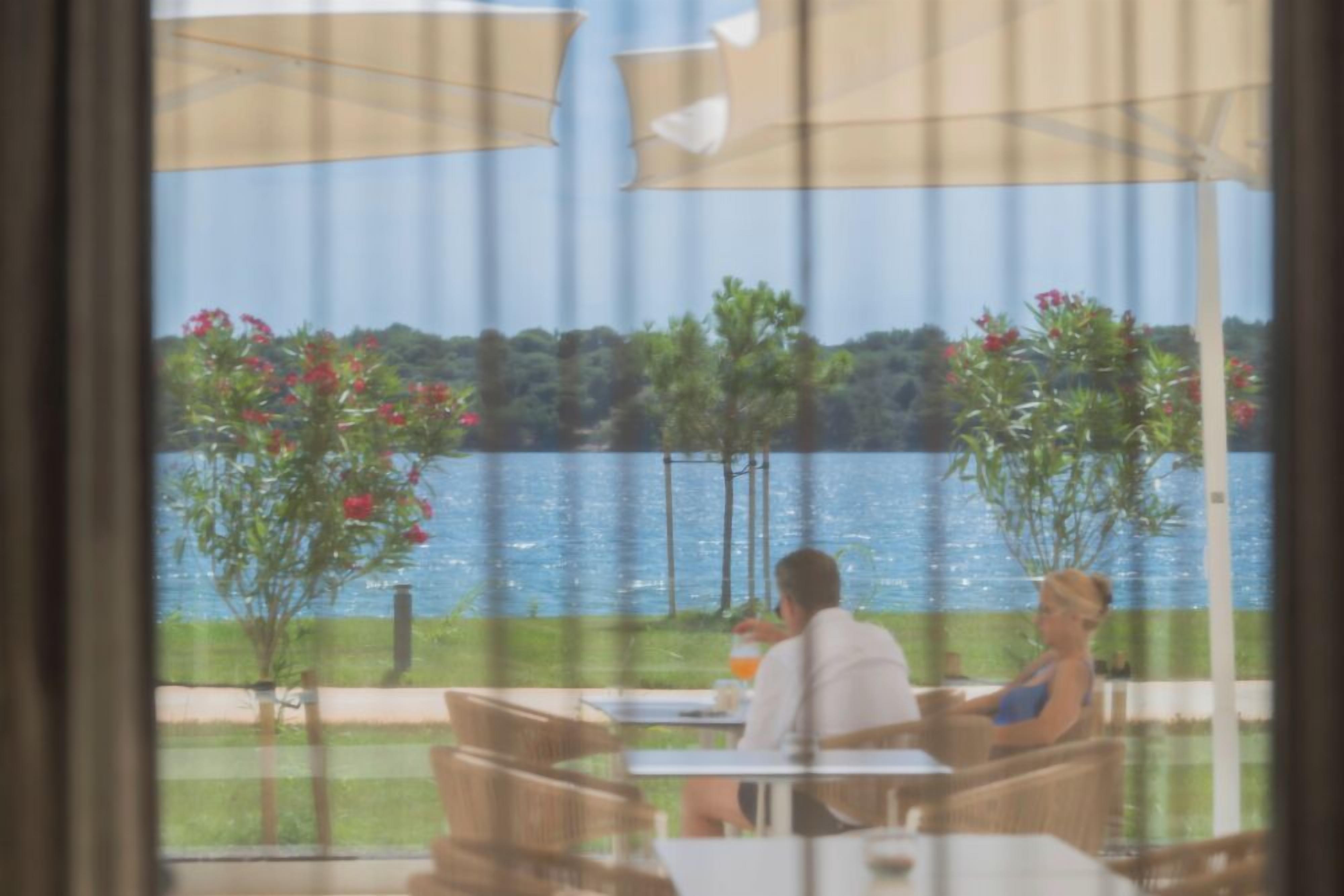An outdoor seating area with tables and chairs, overlooking a body of water and greenery.
