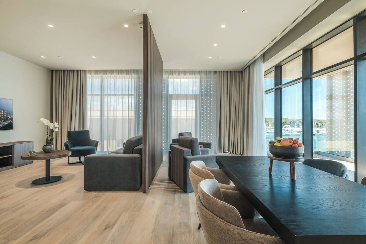 Un salon moderne avec un coin repas, de grandes fenêtres et une vue sur l’extérieur.