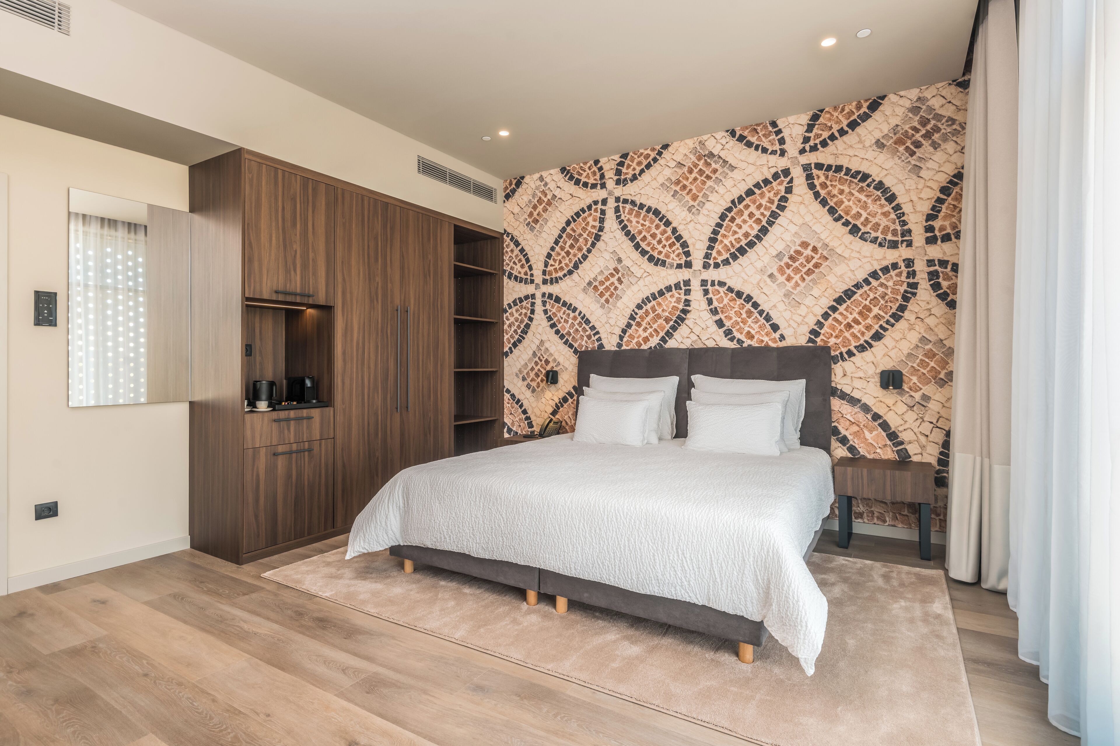 A bedroom with a bed, wooden wardrobe, built-in shelves, and a patterned wall.