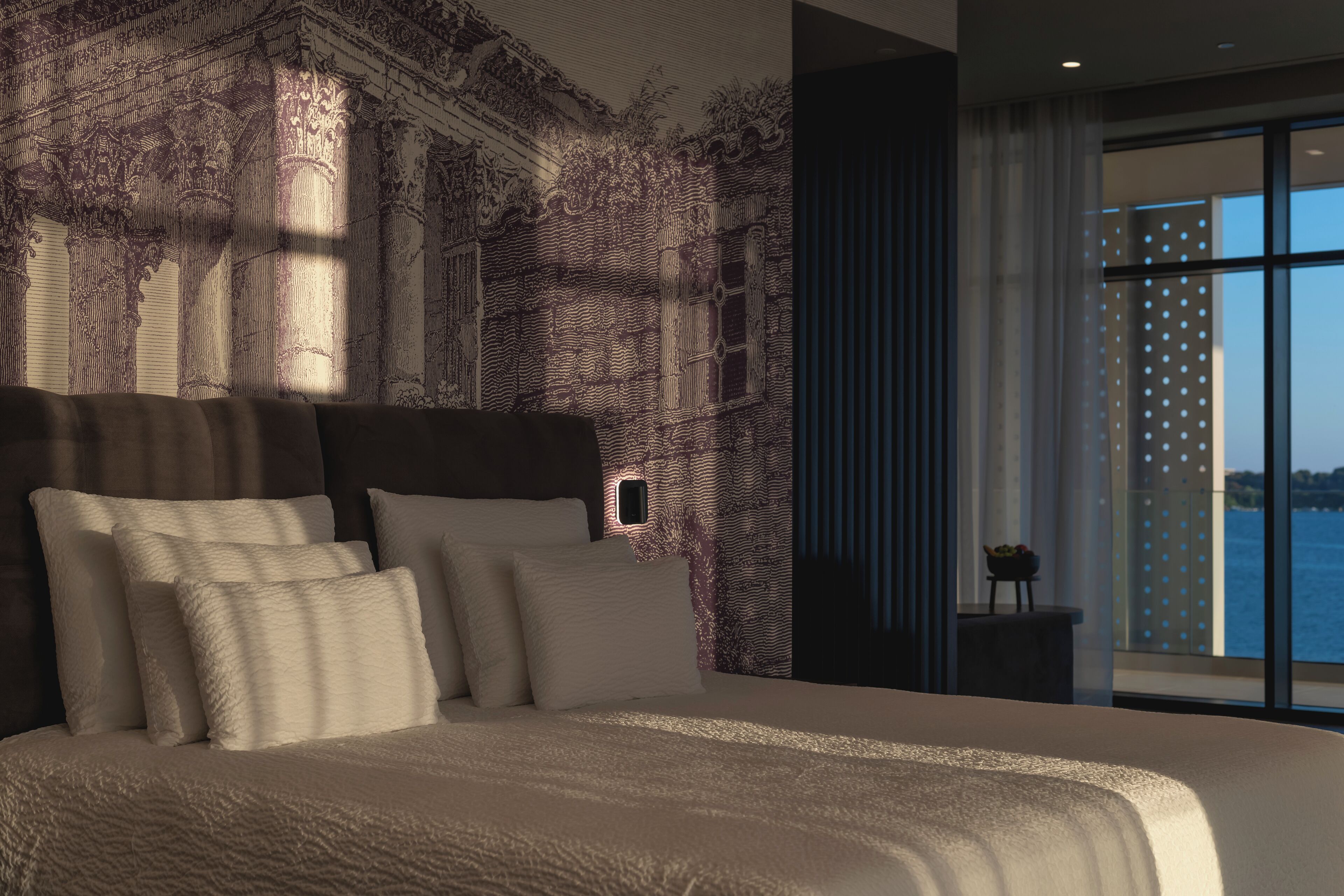 Un dormitorio moderno con una cama grande, un mural en la pared y vistas al agua.