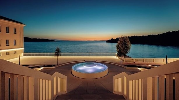 Un hotel con una piscina circular en el centro, rodeada por una escalera que conduce a una terraza con vistas a un cuerpo de agua.
