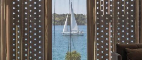 Una habitación con vistas a un velero en el agua, visible a través de una ventana con cortinas de lunares.