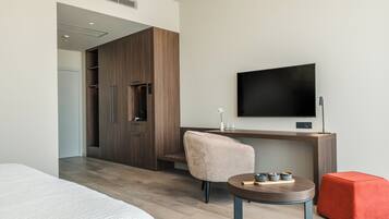 Una habitación de hotel moderna con cama, escritorio con silla, televisión y una mesita con objetos decorativos.