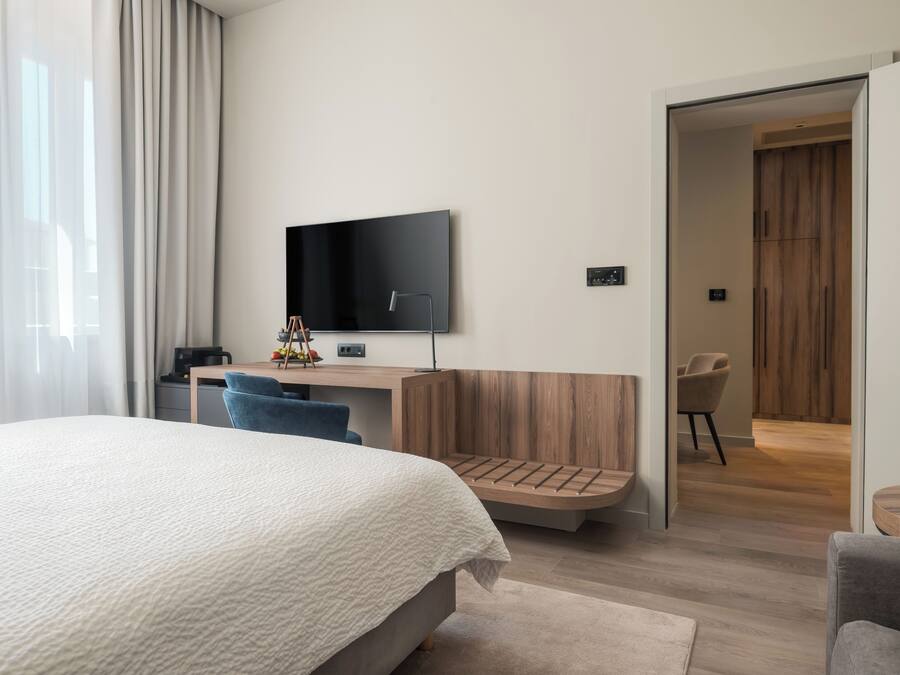 Una habitación de hotel moderna con una cama grande, un escritorio con televisor de pantalla plana, un banco de madera y una silla.
