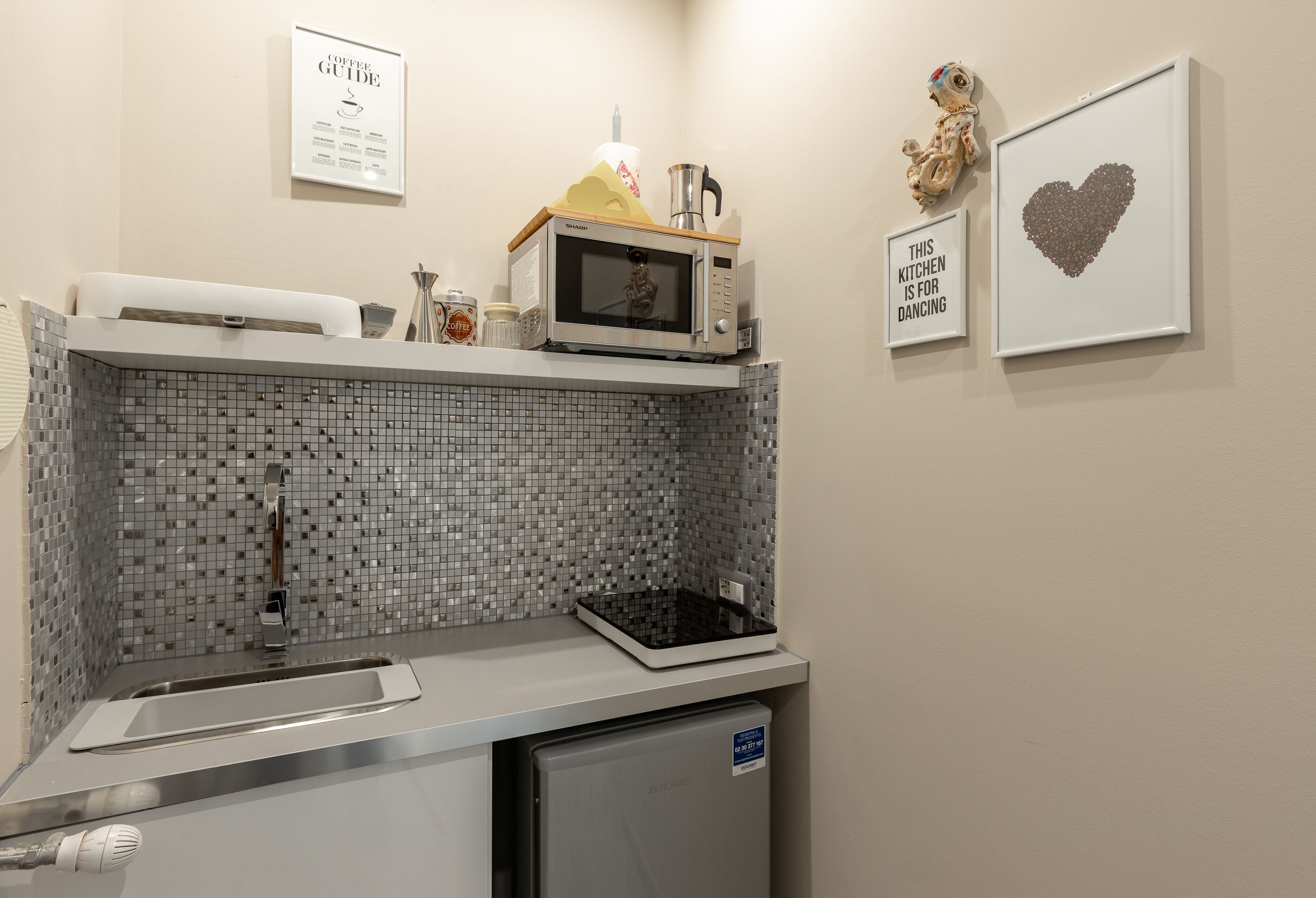 A compact kitchen with a microwave, sink, and a refrigerator. There are decorative items and framed pictures on the wall.