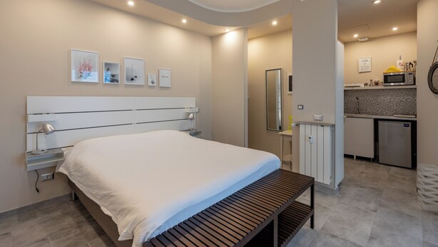 A modern bedroom with a large bed, bedside tables, a bench, and a kitchenette in the background. - Cerisola lovely studios in Rapallo (Rapallo)