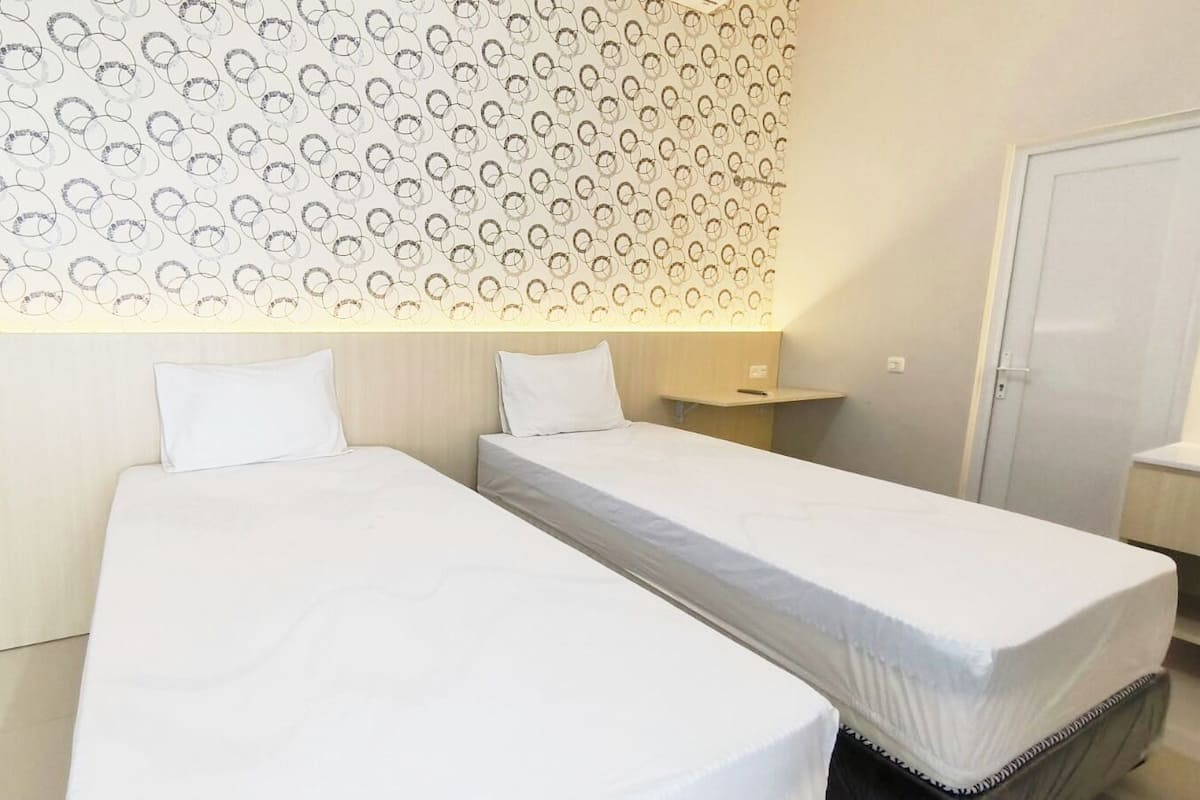 A hotel room with two single beds, a bedside table, a nightstand, and a patterned wall.